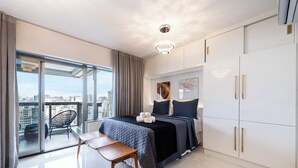 Une chambre moderne avec un grand lit, un bureau et une chaise. Elle offre une vue sur la ville grâce à de grandes fenêtres.