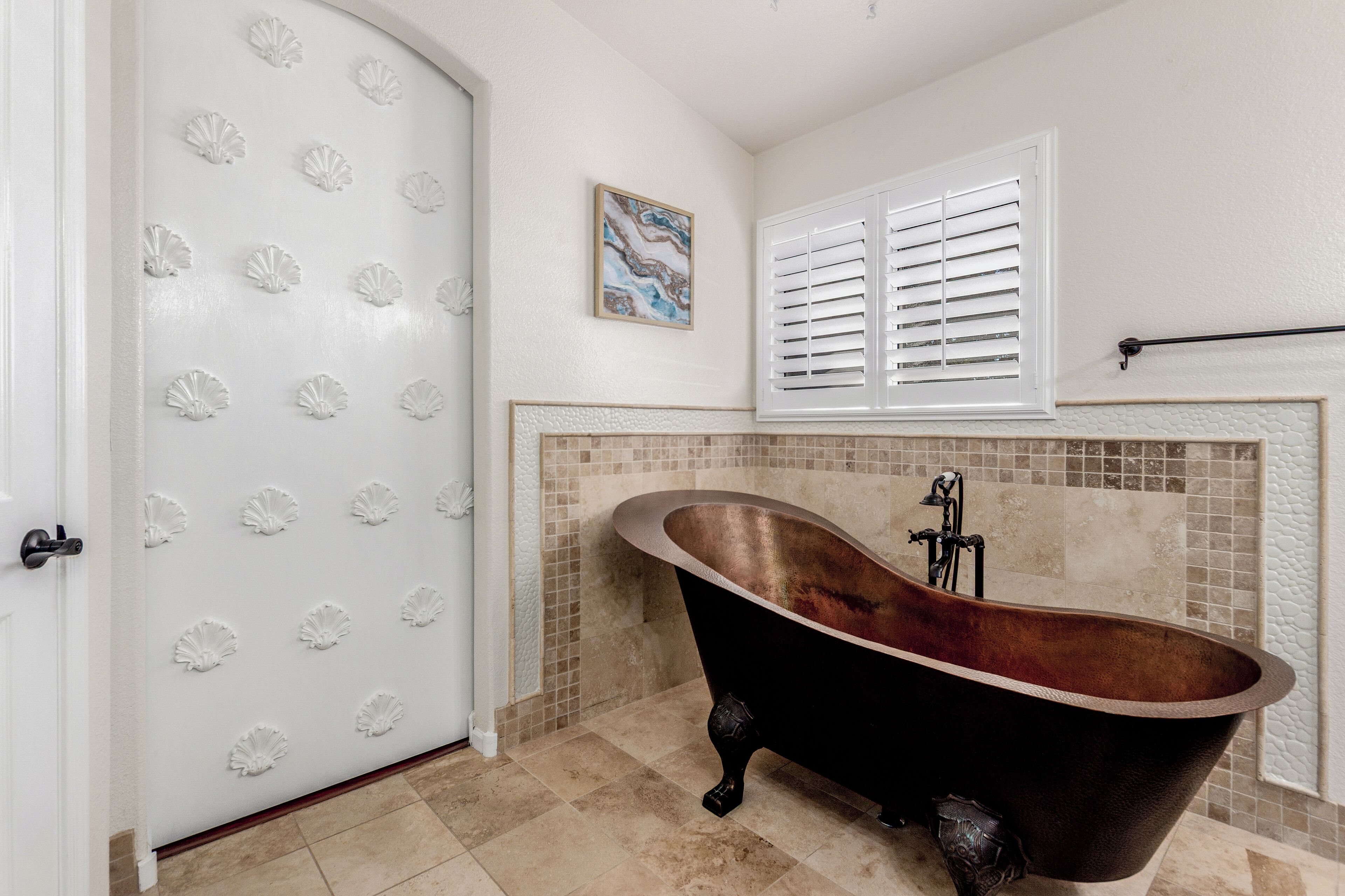 Een badkamer met een vrijstaand bad, een betegelde douche en een deur met decoratieve schelpmotieven.