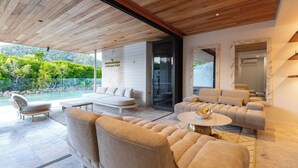 Un espace de vie moderne avec un plafond en bois, un grand canapé, une table basse et une porte en verre donnant sur une piscine.