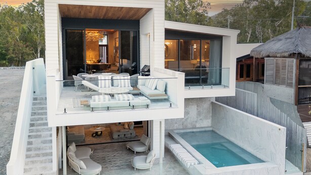 A modern multi-level house with a glass balcony, outdoor seating, and a swimming pool.