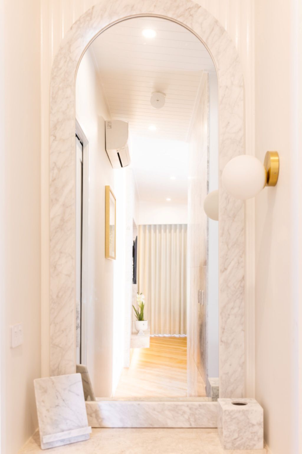 A hallway with a marble floor, a mirror, a door with a golden handle, and a small plant.