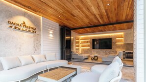 A modern living room with a sectional sofa, a coffee table, and a flat-screen TV mounted on the wall.