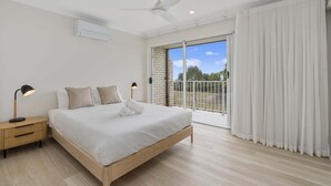 A bedroom with a bed, bedside lamps, a ceiling fan, and a view through a sliding glass door to the outside.