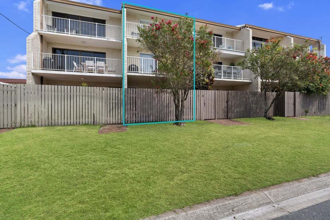 A two-story apartment building with a fenced yard, a small tree, and a balcony.