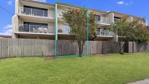 A two-story apartment building with a fenced yard, a small tree, and a balcony.