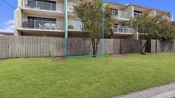 A two-story apartment building with a fenced yard, a small tree, and a balcony.