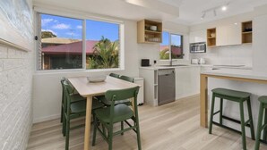 A modern kitchen with a dining area, large windows, and a view of a red-roofed building.