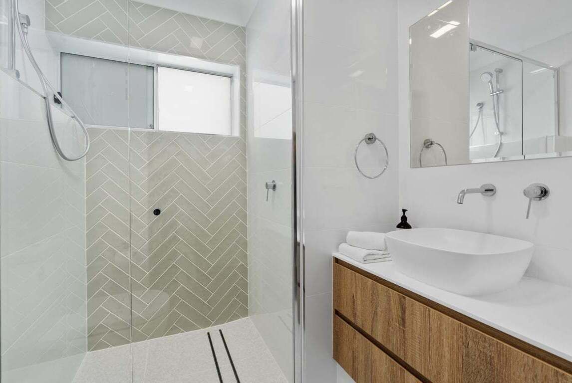 A modern bathroom with a glass shower enclosure, a white sink with a wooden vanity, and a large mirror above the sink.