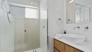 A modern bathroom with a glass shower enclosure, a white sink with a wooden vanity, and a large mirror above the sink.