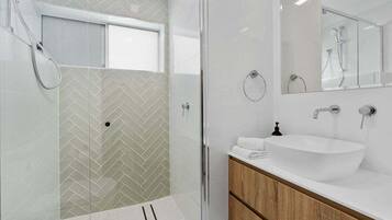 A modern bathroom with a glass shower enclosure, a white sink with a wooden vanity, and a large mirror above the sink.