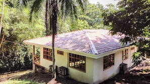 Una pequeña casa de un piso con techo de tejas, rodeada de densa vegetación tropical.