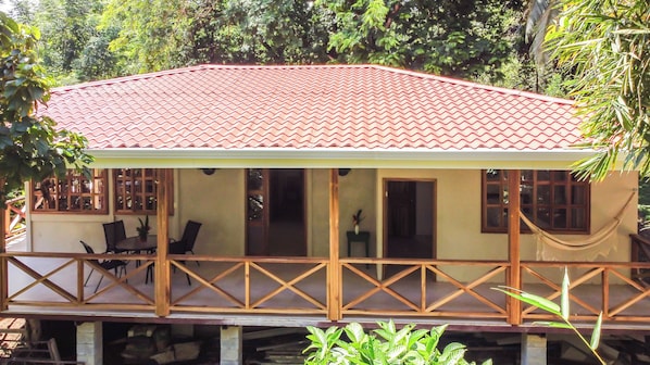 Una casa de dos pisos con techo de tejas rojas, barandilla de balcón de madera y un área de comedor con sillas y una mesa.