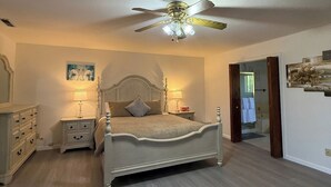 Quarto com cama, mesas de cabeceira, ventilador de teto e porta para um banheiro.