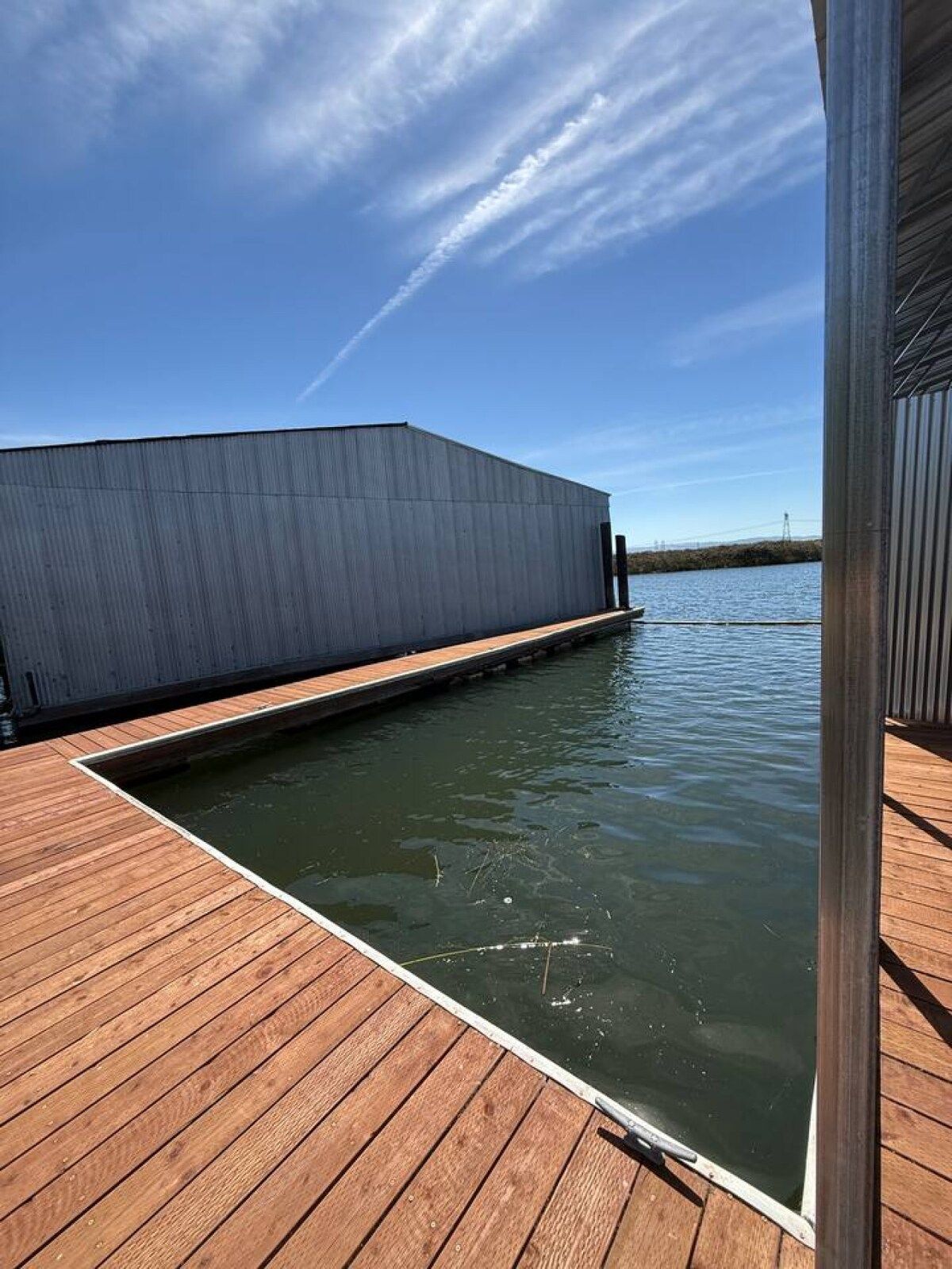 Une terrasse en bois qui mène à un plan d’eau, avec un grand bâtiment industriel en arrière-plan.
