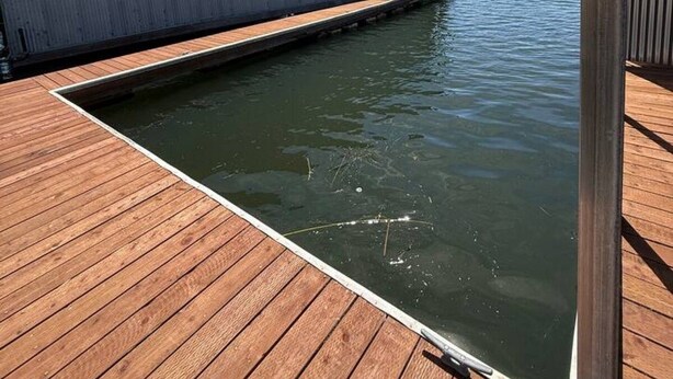 A wooden deck leading to a body of water with a large industrial building in the background. - Newly Renovated Lakefront w/Dock (Bethel Island)