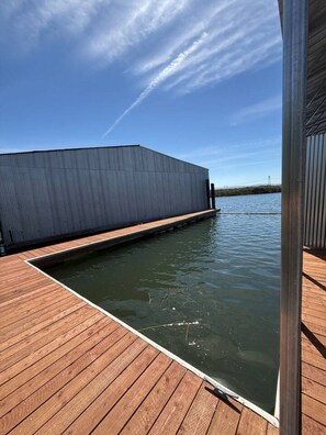 Una terraza de madera que conduce a una masa de agua, con un edificio industrial grande al fondo.