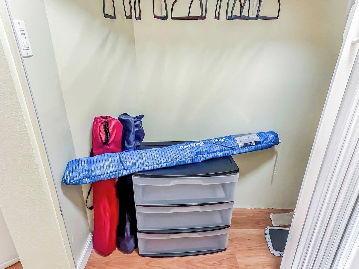 A room with a bed, a wall-mounted shelf with bags, and a set of drawers.