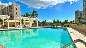 A swimming pool with a clear blue water, surrounded by lounge chairs and umbrellas, with tall buildings in the background. - Charming Twin-Joined Studio with Plentiful Space (Honolulu)