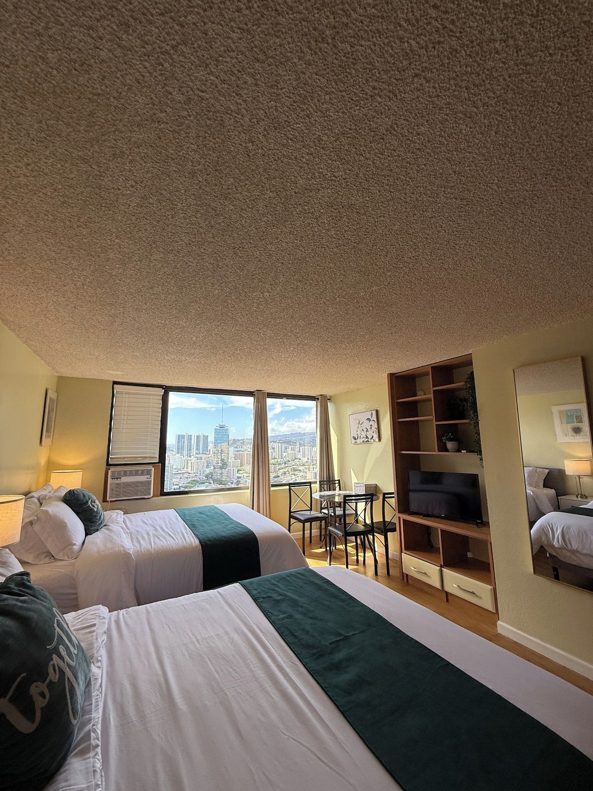 Ein Hotelzimmer mit zwei Betten, einem Esstisch, einem Fernseher und Blick auf die Stadt.