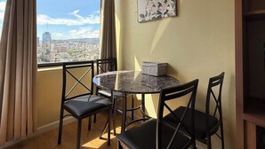 A room with a round table and four chairs, a window with curtains, a city view, and a framed picture on the wall. - Charming Twin-Joined Studio with Plentiful Space (Honolulu)