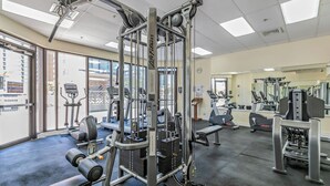 Un gimnasio con diferentes máquinas de ejercicio, incluyendo una máquina de poleas, cintas de correr y bancos de pesas.