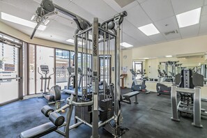 Un gimnasio con diferentes máquinas de ejercicio, incluyendo una máquina de poleas, cintas de correr y bancos de pesas.