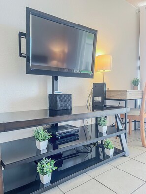 A flat-screen TV mounted on a wall, a desk with a lamp, and a chair.
