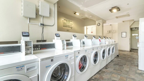 A laundry facility with multiple washing machines and dryers, a control panel, and a safety sign on the wall. - A Clean Homie Getaway, Double Bed Studio 2 a VIEW (Honolulu)