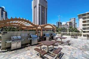 An outdoor patio with barbecue grills, tables, and a pergola.