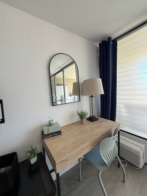 A modern room with a wooden desk, a chair, a lamp, a mirror, and a window with curtains.