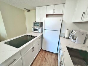 A compact kitchen with a built-in stove, a microwave, a refrigerator, and a coffee maker.