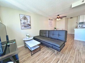 A living room with a sofa, a coffee table, a television, and a ceiling fan. - Comfy and Modern Condo By Waikiki! (Honolulu)