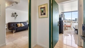 Una habitación con un sofá negro, un cuadro en la pared y vistas a un paisaje urbano a través de un ventanal amplio.