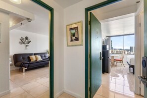 Una habitación con un sofá negro, un cuadro en la pared y vistas a un paisaje urbano a través de un ventanal amplio.