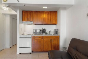 Una cocina compacta con armarios de madera, un microondas, una estufa y una cafetera.