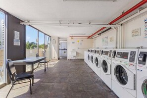 Un cuarto de lavandería con varias lavadoras, una mesa con sillas y vistas a través de puertas de vidrio.