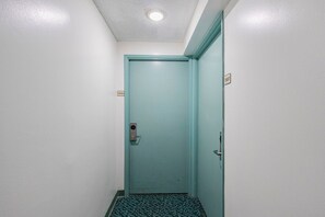 A narrow hallway with a teal door, a patterned carpet, and a ceiling light. - Skyline Island Stay • Two Adjoining Studios (Honolulu)
