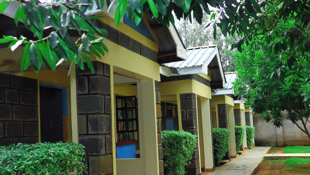 A row of rooms with stone walls and yellow trim, connected by a covered walkway. - Ole Polos Resort Mogotio  (Mogotio)