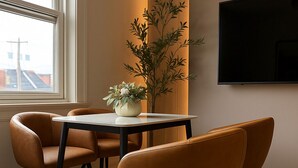 Ett modernt matområde med ett runt bord, två stolar, en krukväxt och en platt-TV som är monterad på väggen.