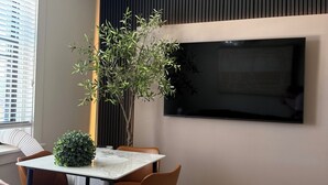 Un espace repas moderne avec une table en marbre, des chaises en cuir, une plante en pot et un grand téléviseur à écran plat fixé au mur.