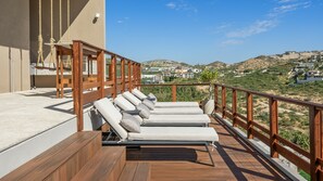 A deck with wooden railings, multiple lounge chairs, and a view of a hilly landscape with buildings. - Villa Solara | Panoramic Ocean views & Luxury Mountaun Retreat villa (San Jose del Cabo)