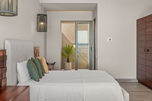 A bedroom with a bed, a bedside table, a potted plant, and a view through a door.