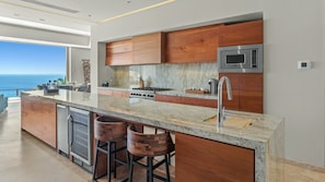A modern kitchen with a large island, stainless steel appliances, and a view of the ocean. - Villa Solara | Panoramic Ocean views & Luxury Mountaun Retreat villa (San Jose del Cabo)