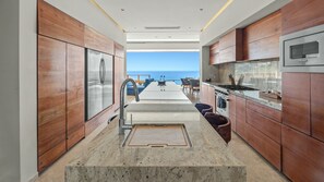 A modern kitchen with a view of the sea, featuring wooden cabinets, stainless steel appliances, and a central island. - Villa Solara | Panoramic Ocean views & Luxury Mountaun Retreat villa (San Jose del Cabo)
