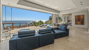 A modern living room with a large sofa, a dining area, and a view of the ocean.
