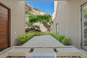 A pathway leading to a building with a wooden door on the left and a glass door on the right. - Villa Solara | Panoramic Ocean views & Luxury Mountaun Retreat villa (San Jose del Cabo)