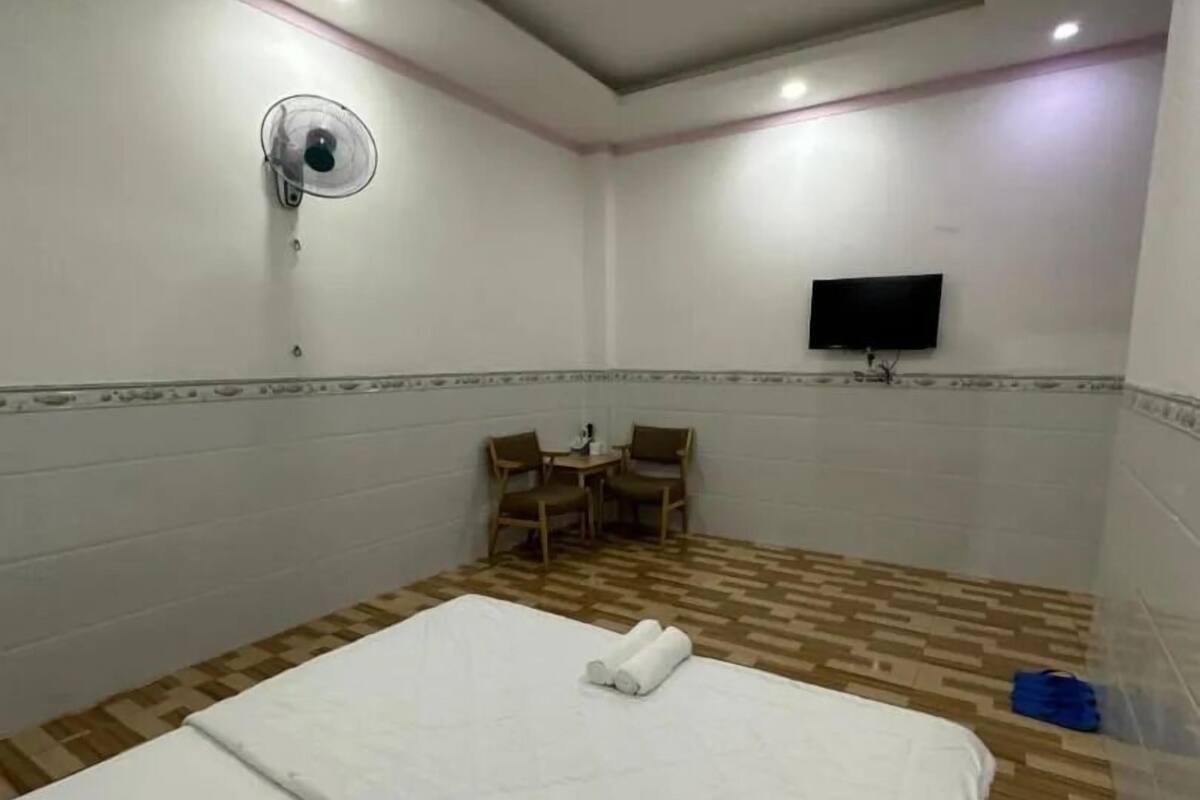 A hotel room with a bed, a desk, two chairs, a flat-screen TV, and a ceiling fan.
