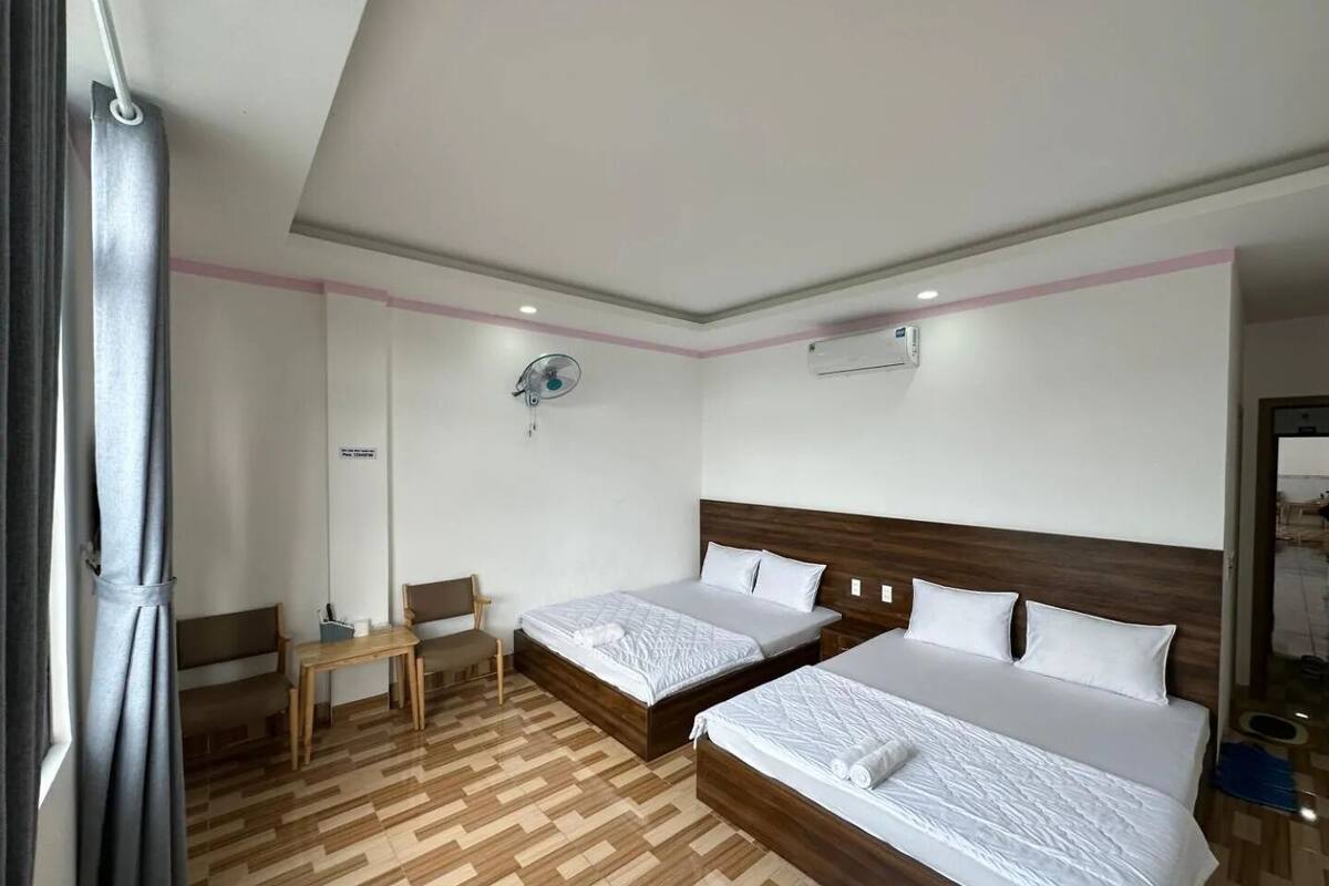 A hotel room with two beds, a small table, a chair, and an air conditioning unit.