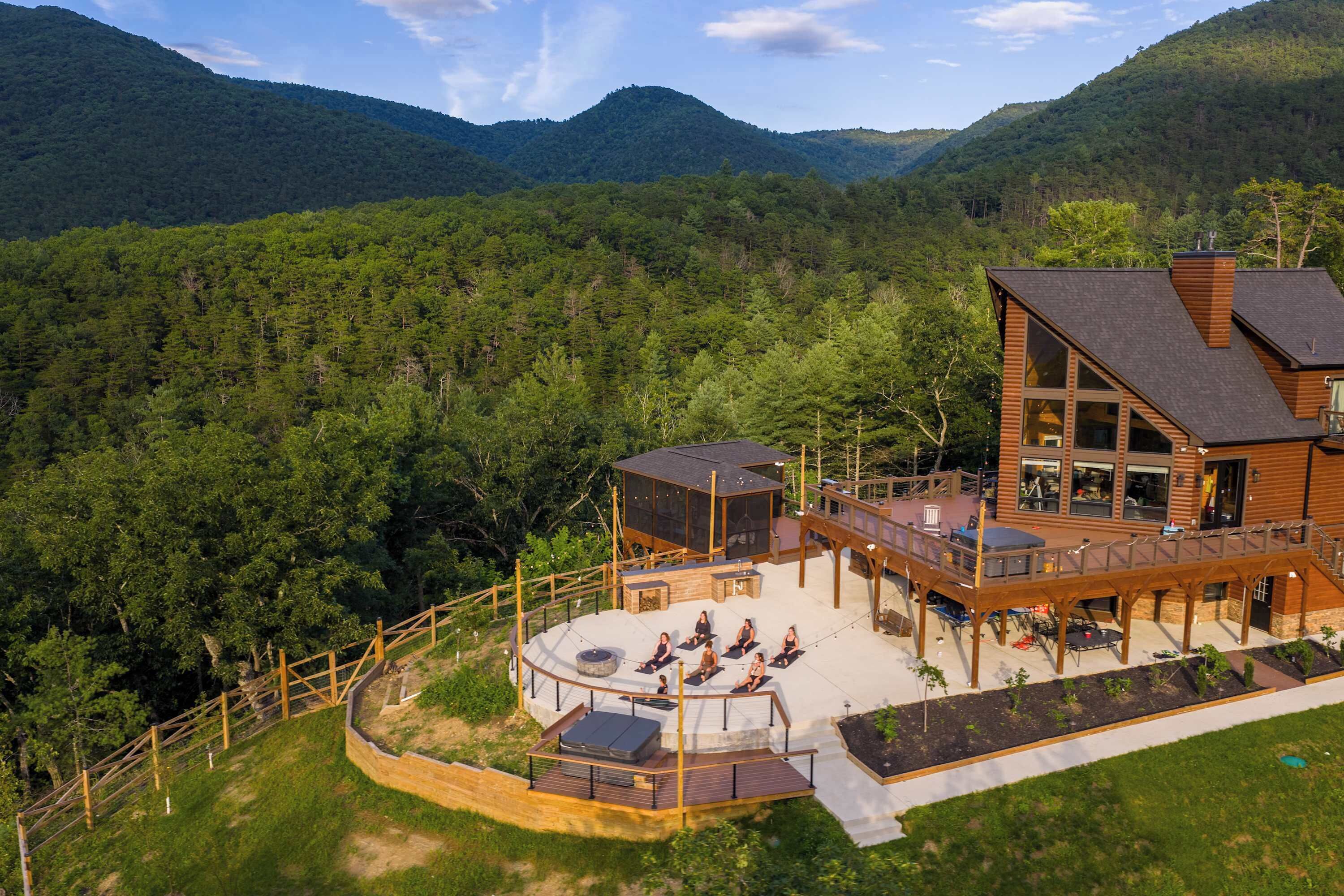 A wooden cabin with a deck, outdoor seating, and a view of a forested mountain.