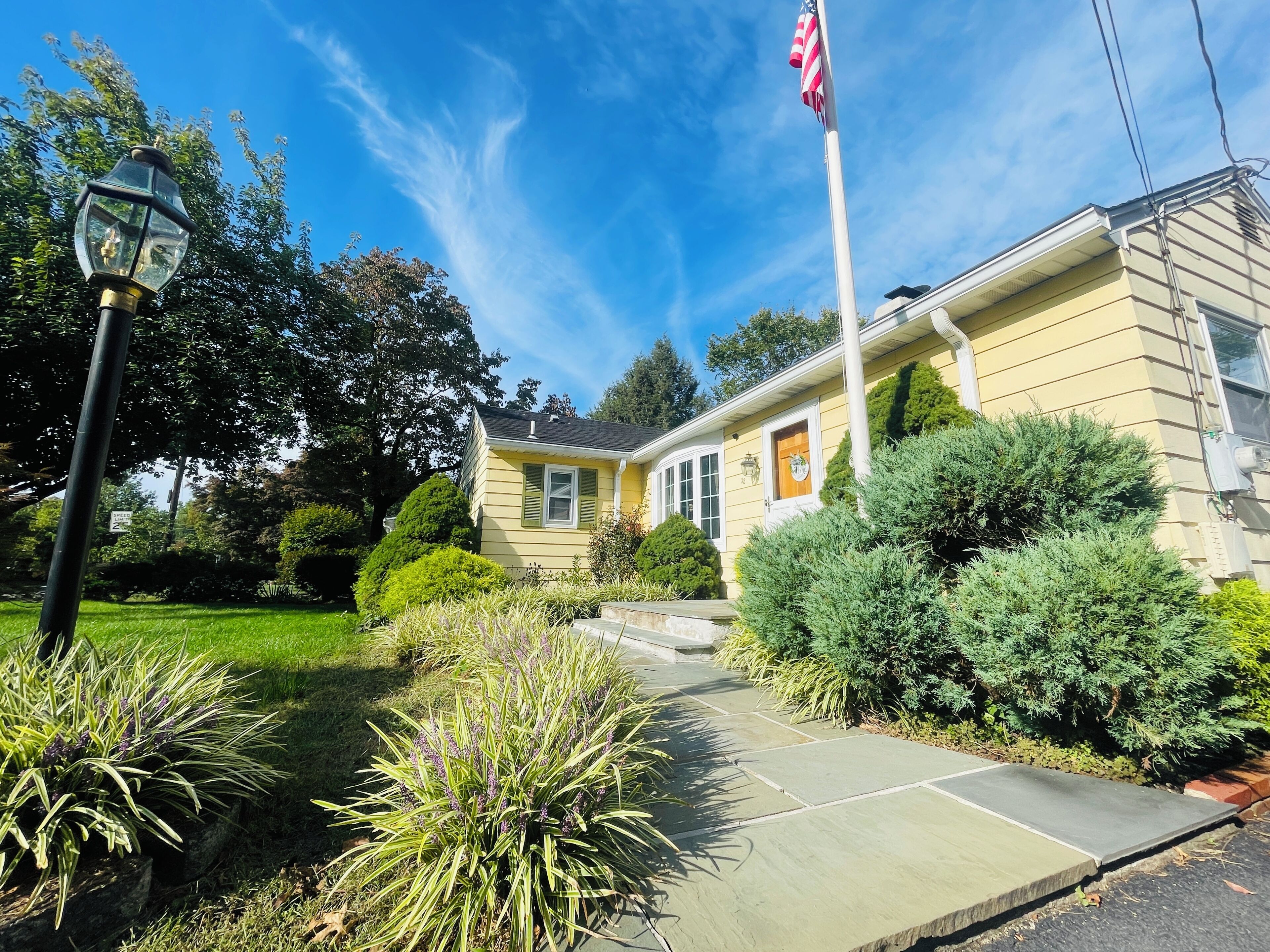 A yellow house with a front yard, a flag, and a street lamp.